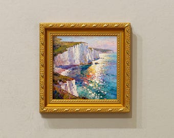 May include: A framed oil painting depicts white cliffs meeting the sea under a colorful sky. The artwork is in a gold ornate frame, adding a touch of elegance. The painting's vibrant colors and detailed brushstrokes capture the natural beauty of the coastal landscape.