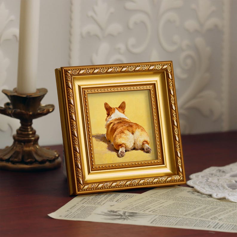 Pu&ograve; includere: Una cornice dorata con un'immagine di un cane corgi visto da dietro, su sfondo giallo. La cornice &egrave; decorata con dettagli ornamentali.