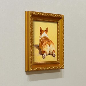 Pu&ograve; includere: Un dipinto incorniciato di un cane corgi visto da dietro, con il suo pelo marrone e bianco e la sua coda soffice. Il dipinto &egrave; ambientato su uno sfondo giallo e si trova in una cornice dorata ornata.