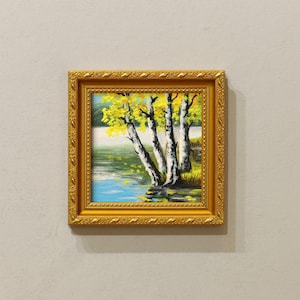 Op de afbeelding: Vierkant ingelijst schilderij van een meerlandschap met berken en gele bladeren. Het schilderij heeft een gouden, sierlijke lijst. Het water is blauw met gele bladeren die op het oppervlak drijven. De lucht is lichtblauw.