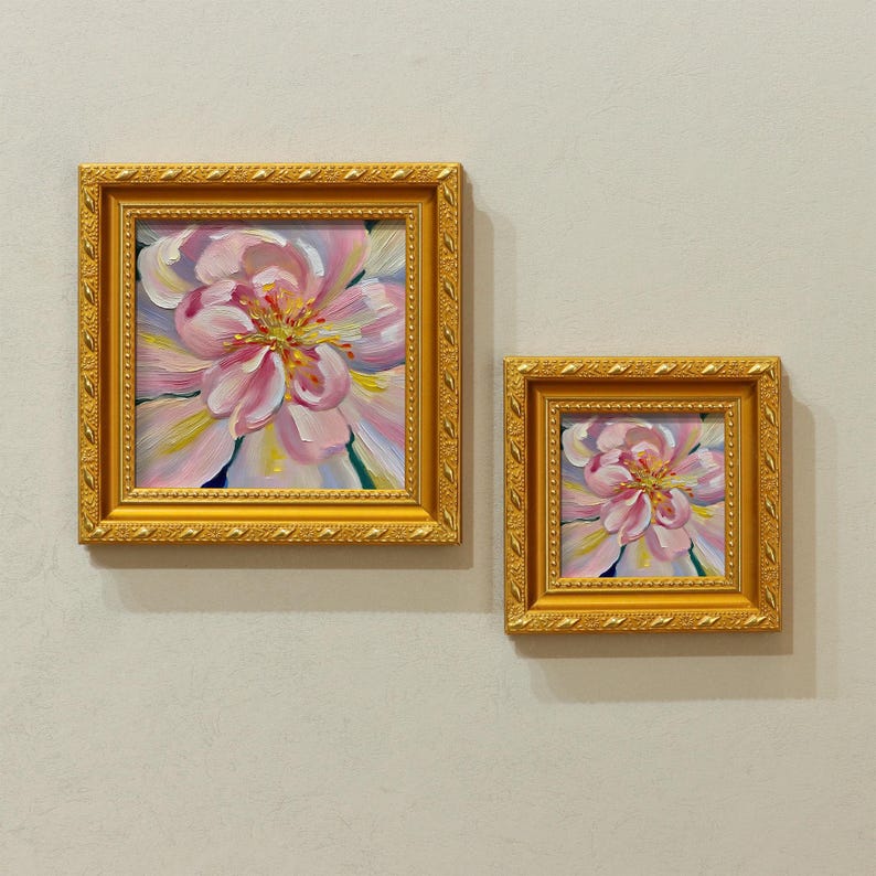 May include: Two framed floral paintings. The larger painting features a close-up of a pink and yellow flower with a detailed center. The smaller painting mirrors the larger one. Both are in ornate gold frames.