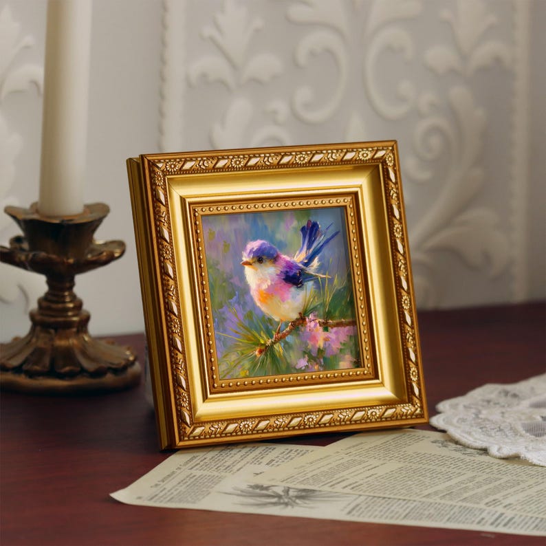 Puede incluir: Pintura enmarcada de un p&aacute;jaro colorido posado en una rama. La obra de arte presenta un marco dorado ornamentado y una vibrante paleta de azules, morados y rosas. La pintura se exhibe sobre una superficie de madera.