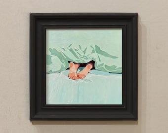 May include: A framed painting shows a person's feet emerging from beneath a light green blanket. The bedsheets are a matching light blue. The artwork is framed in a black, rectangular frame.