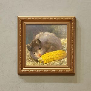 May include: A framed oil painting depicts a hamster with gray fur and a pink nose, nestled beside a bright yellow ear of corn. The painting is set in a gold ornate frame, creating a classic and detailed artwork.