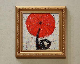 Op de afbeelding: Een vierkant schilderij in een sierlijke gouden lijst met een grote, felrode paraplu vastgehouden door een donker silhouet. De achtergrond is een lichtgrijs oppervlak bedekt met verspreide, veelkleurige verfspatten in blauw, geel en groen.