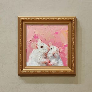 May include: A framed oil painting featuring two white rats against a pink and peach background. The artwork is in a gold ornate frame, adding a touch of elegance. The painting's style is impressionistic, with visible brushstrokes.