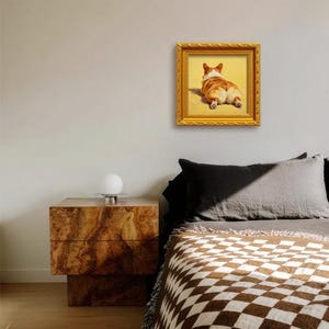 Pu&ograve; includere: Un dipinto incorniciato di un cane corgi, visto da dietro, con una cornice dorata. Il dipinto &egrave; appeso a una parete chiara sopra un letto con una coperta fantasia e un comodino in legno.
