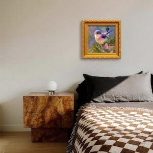 Puede incluir: Pintura enmarcada de un p&aacute;jaro azul posado en una rama. La obra de arte presenta un marco dorado y est&aacute; colgada en una pared sobre una cama. El p&aacute;jaro tiene plumas azules, moradas y naranjas.