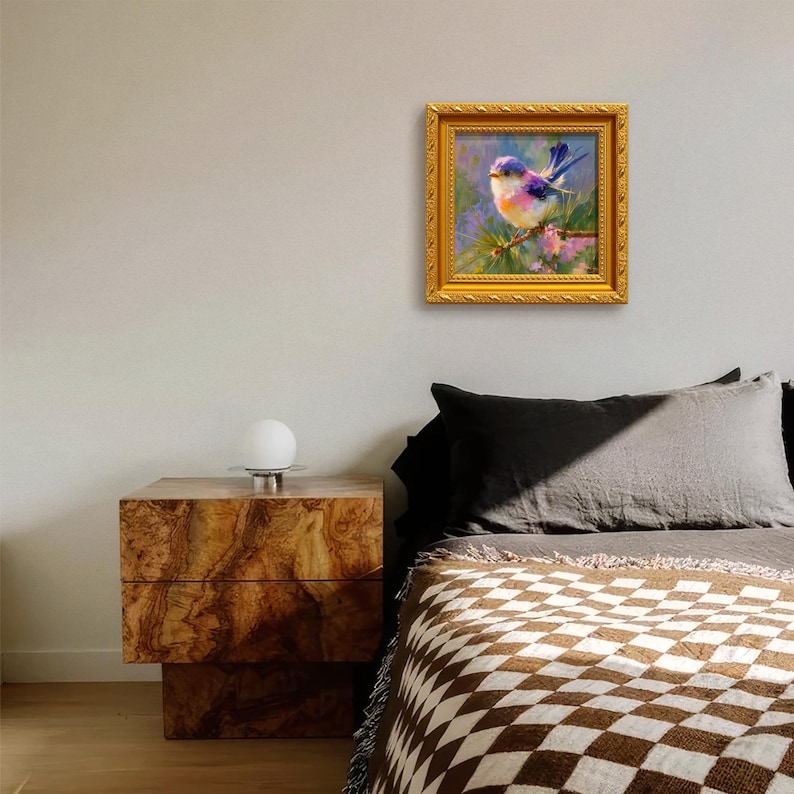 Puede incluir: Pintura enmarcada de un p&aacute;jaro azul posado en una rama. La obra de arte presenta un marco dorado y est&aacute; colgada en una pared sobre una cama. El p&aacute;jaro tiene plumas azules, moradas y naranjas.
