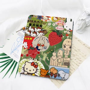 May include: A colorful tablet case featuring a collage of cartoon characters, strawberries, and Japanese text. The design includes Hello Kitty, a bunny, and other whimsical illustrations on a white background.