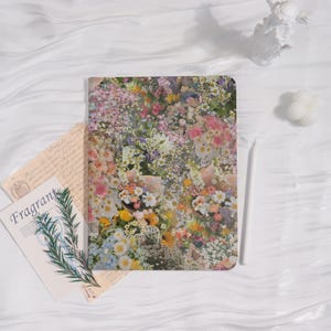 May include: A floral-patterned notebook with a white stylus and the word "Fragrant" on a card. The notebook features a collage of colorful flowers in shades of pink, yellow, and white. The background is a white, textured surface.