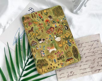 May include: A green, yellow, and brown notebook cover with a whimsical illustration of a village scene. The illustration features houses, animals, flowers, and other details.