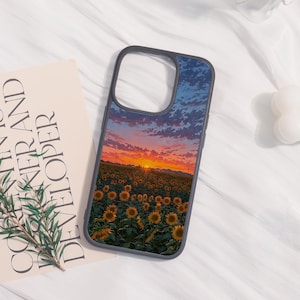 May include: A black phone case featuring a vibrant sunset over a sunflower field. The design showcases a bright orange sun setting behind the sunflowers, with a blue and orange sky. The case is next to a book with the text "CORNER AND DEVELOPER".