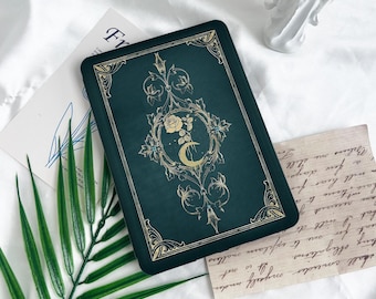 May include: A green journal with a gold design featuring a crescent moon and a rose. The journal has a decorative border and a vintage aesthetic.