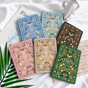 May include: A collection of six rectangular notebooks featuring floral patterns in blue, light blue, black, pink, beige, and green. Each notebook has a decorative border and a central arrangement of small flowers, leaves, and stems on the front cover.