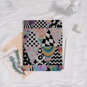 May include: A patterned tablet case featuring a patchwork design of triangles with diverse patterns, including polka dots and checkerboards. A white stylus lies beside the case. A card with the word "Fragrant" is also visible. The case is likely 20-25 cm in length.
