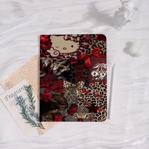 May include: A decorative notebook with a collage design. The design includes a Hello Kitty illustration, leopard print, red bows, cherries, and the text "Fuck Humdrum Things". The notebook has a rectangular shape.