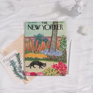 May include: A copy of The New Yorker magazine from June 18, 1960, featuring a colorful illustration of a black cat walking through a garden. The cover art includes a brick wall, flowers, and a tree. The magazine is surrounded by other decorative items.