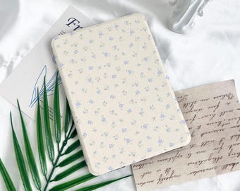 May include: A cream-coloured phone case with a floral pattern of small blue flowers. The case is on a white background with a fern and a vintage letter. The word "FR" is visible on a card. The case is rectangular.