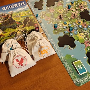 Puede incluir: Un tablero de juego con un mapa azul y verde, fichas hexagonales negras y piezas de juego blancas y azules. Hay cuatro bolsas de tela blancas con diferentes símbolos de colores. El tablero de juego tiene el texto "SCOTLAND" impreso en él. La caja del juego de mesa "REBIRTH" es visible en el fondo.