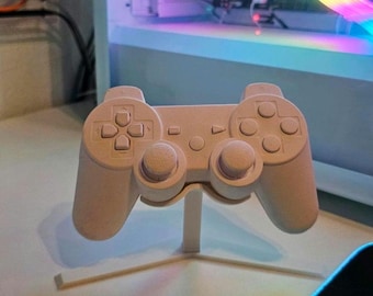 May include: A white plastic video game controller on a white stand. The controller has a standard layout with buttons, joysticks, and a directional pad.