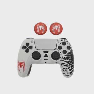 May include: White and black gaming controller featuring red spider emblems. The controller has a white central panel, black buttons, and a black and white web design on the right. Two red thumb grips with white spider logos are above.