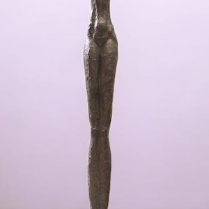 Puede incluir: Una escultura de bronce de una figura esbelta con los brazos levantados por encima de la cabeza. La escultura tiene una superficie texturizada y se apoya sobre una base cuadrada. La forma de la figura es alargada y detallada.