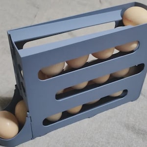 May include: A blue plastic egg holder with multiple slots, filled with beige eggs. The holder is designed to store and dispense eggs, keeping them organized. The design allows for easy access and visibility of the eggs.