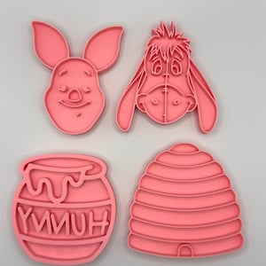 Pode incluir: Quatro cortadores de biscoitos cor-de-rosa com personagens e s&iacute;mbolos de uma hist&oacute;ria infantil popular. O conjunto inclui uma cara de coelho, uma cara de burro, um pote de mel com a palavra "YMMUH" e uma colmeia.