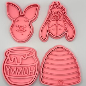 Pode incluir: Quatro cortadores de biscoitos cor-de-rosa em forma de coelho, burro, pote de mel com a palavra "YMMUH" e colmeia. Estes cortadores de pl&aacute;stico s&atilde;o projetados para assar biscoitos.