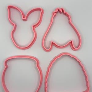 Pode incluir: Quatro cortadores de biscoitos de pl&aacute;stico rosa em v&aacute;rias formas. As formas incluem uma cabe&ccedil;a de coelho, uma abelha, um pote de mel e uma colmeia. Os cortadores de biscoitos s&atilde;o feitos de pl&aacute;stico rosa s&oacute;lido e s&atilde;o colocados em um fundo branco.