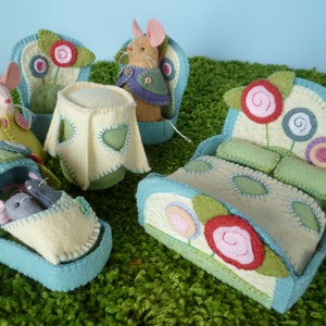 Op de afbeelding: Een set van vilten speelgoedmeubels voor een poppenhuis of een speelset, inclusief een bed, een stoel, een tafel en een wieg. De meubels zijn versierd met kleurrijke bloemen en swirls. De meubels zijn gemaakt van vilt en zijn met de hand genaaid.