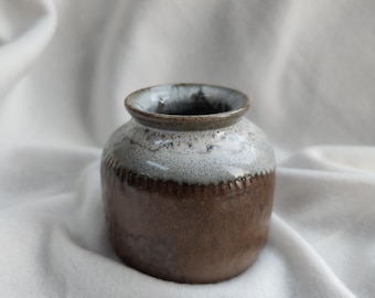 May include: A small, brown ceramic vase with a white glaze on the top half. The vase has a rounded body and a slightly flared lip.