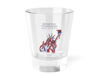 May include: A clear glass shot glass featuring a graphic of the Statue of Liberty in red, white, and blue. Above the graphic, the text reads America 250 YEARS in a dark blue font. The glass has a thick base and a tapered cylindrical shape.
