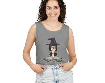 May include: A grey sleeveless tank top featuring a graphic of a cartoon character wearing a black witch hat with a purple band, black glasses, and holding a lit candle while reading an open book. The text "Witch Please" is printed below the graphic.