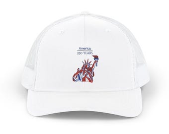 May include: A white trucker hat featuring a graphic of the Statue of Liberty in red, white, and blue. Above the graphic, the text reads America 250 YEARS in blue. The cap has a solid front panel and a mesh back panel with a curved brim.