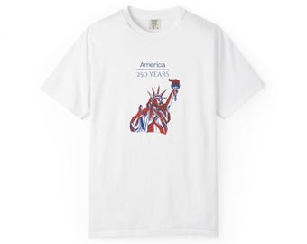 May include: A white short-sleeve t-shirt featuring a graphic of the Statue of Liberty in red and blue lines. Above the graphic, the text reads America 250 YEARS in a dark blue font. The shirt has a crew neckline and a standard fit design.