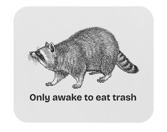 May include: A rectangular mouse pad with a white background featuring a black and white line art illustration of a raccoon. Below the raccoon, the text "Only awake to eat trash" is printed in a bold, black, sans-serif font.
