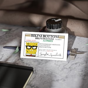 Może przedstawiać: Biało-żółta karta identyfikacyjna Bikini Bottom z kreskówkowym wizerunkiem SpongeBoba Kanciastoportego w okularach. Karta zawiera tekst "Bikini Bottom", "Wygasa 12-11-03" i "SpongeBob Kanciastoporty".