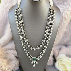 Puede incluir: Un collar de tres hileras con un colgante de piedra verde. El collar est&aacute; hecho de plata y tiene un dise&ntilde;o en blanco y negro. El colgante est&aacute; rodeado de piedras blancas m&aacute;s peque&ntilde;as.
