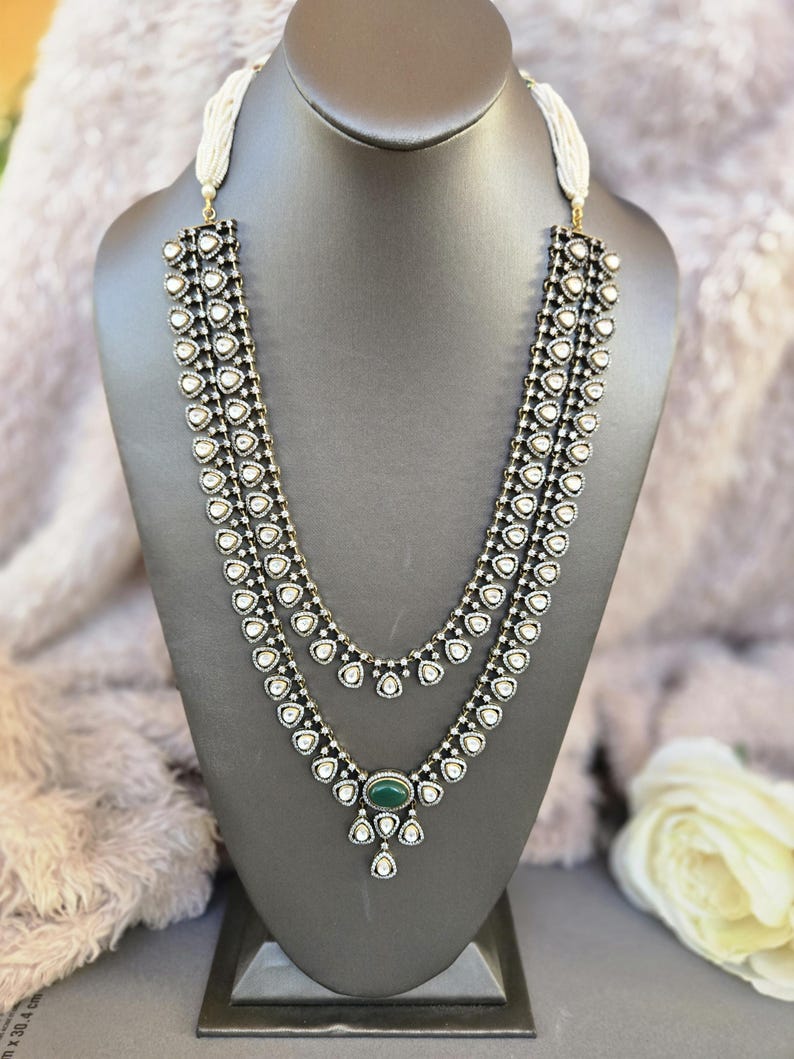 Puede incluir: Un collar de tres hileras con un colgante de piedra verde. El collar est&aacute; hecho de plata y tiene un dise&ntilde;o en blanco y negro. El colgante est&aacute; rodeado de piedras blancas m&aacute;s peque&ntilde;as.