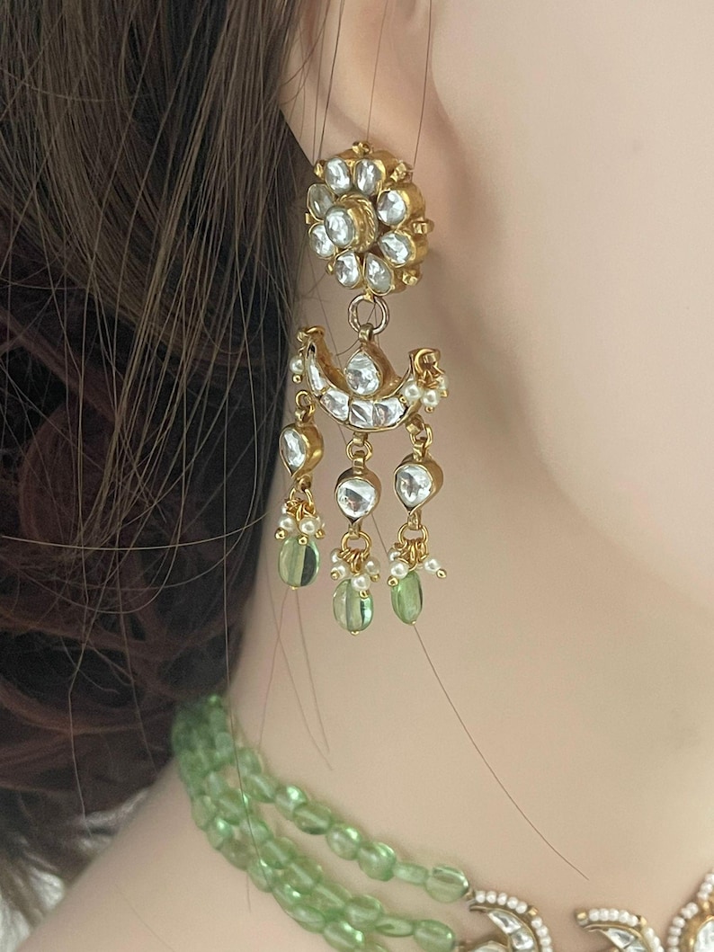 Op de afbeelding: Gouden oorhangers met een bloemmotief en groene en witte stenen.