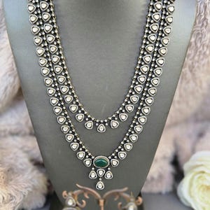 Puede incluir: Un collar de plata de tres hileras con piedras blancas y un colgante de piedra verde. Pendientes a juego con piedras verdes y piedras blancas.