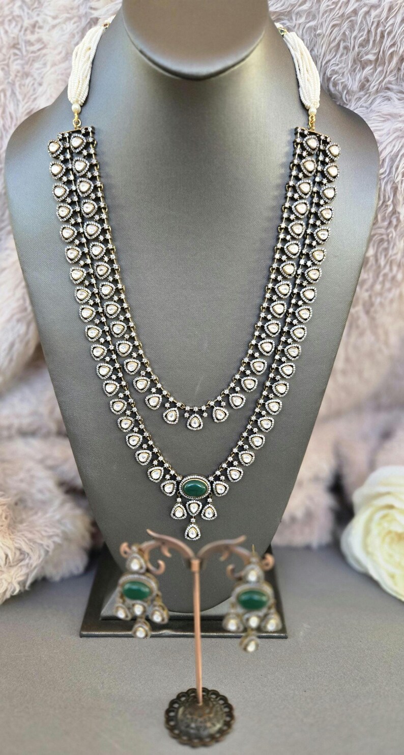 Puede incluir: Un collar de plata de tres hileras con piedras blancas y un colgante de piedra verde. Pendientes a juego con piedras verdes y piedras blancas.
