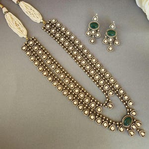 Puede incluir: Un collar de oro de tres hileras con piedras blancas y piedras preciosas verdes. El collar tiene forma de l&aacute;grima y est&aacute; adornado con piedras m&aacute;s peque&ntilde;as. Tambi&eacute;n se incluyen pendientes a juego con piedras preciosas verdes.
