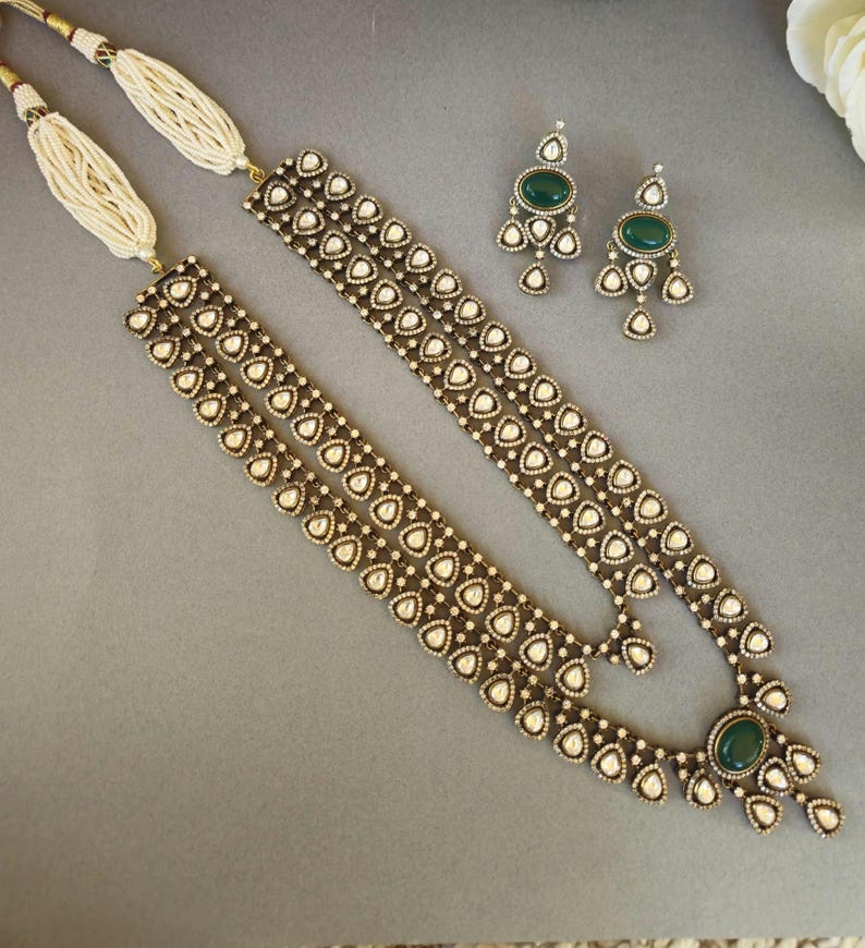 Puede incluir: Un collar de oro de tres hileras con piedras blancas y piedras preciosas verdes. El collar tiene forma de l&aacute;grima y est&aacute; adornado con piedras m&aacute;s peque&ntilde;as. Tambi&eacute;n se incluyen pendientes a juego con piedras preciosas verdes.