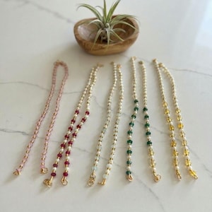 May include: Five beaded necklaces or bracelets arranged in a row. The strands feature small white beads interspersed with faceted colored beads in pink, deep red, clear, emerald green, and yellow. Each piece has a small gold-toned metal clasp.