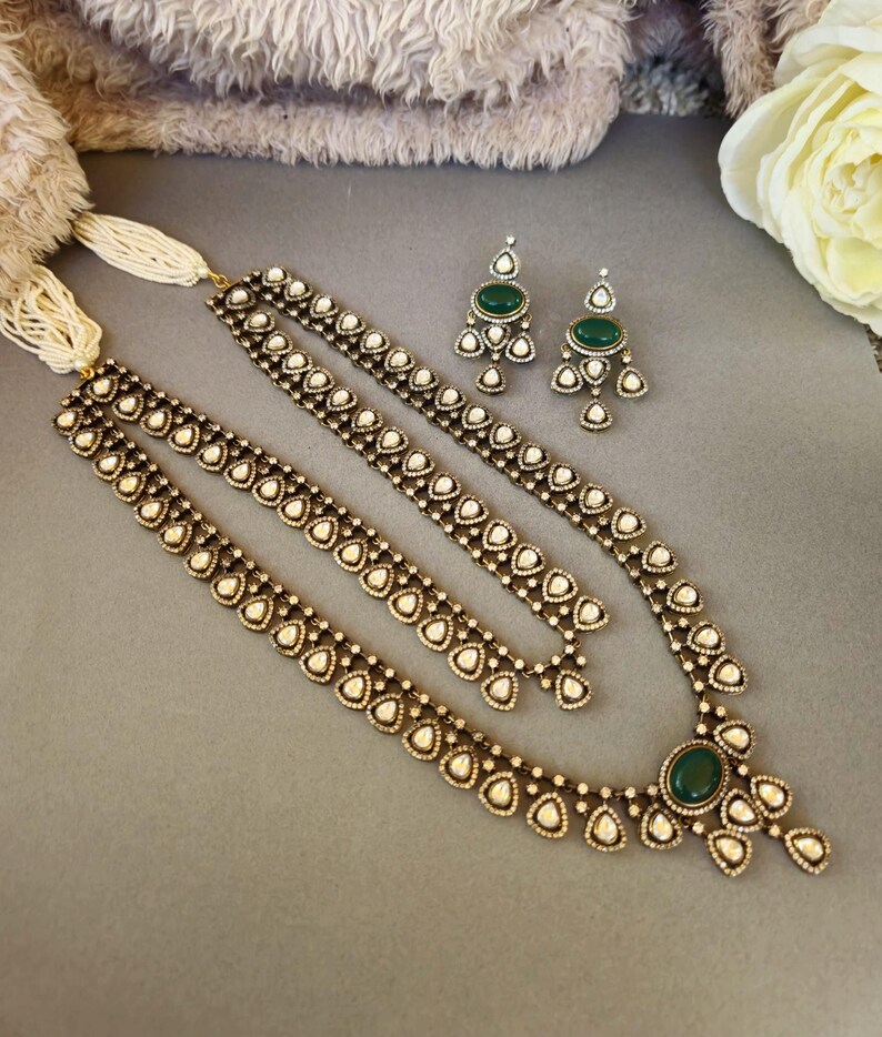 Puede incluir: Un collar de tono dorado con un colgante de piedra verde y detalles de perlas blancas. El collar es de capas y tiene un dise&ntilde;o delicado. Tambi&eacute;n se incluyen pendientes a juego con piedras verdes y perlas blancas.