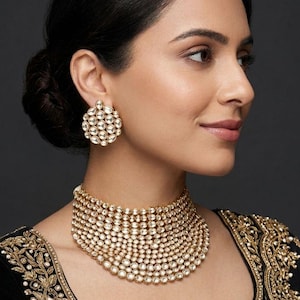 May include: A woman wearing a gold choker necklace and matching earrings. The jewellery is decorated with many small, clear stones. The woman is wearing a black top with gold embroidery.