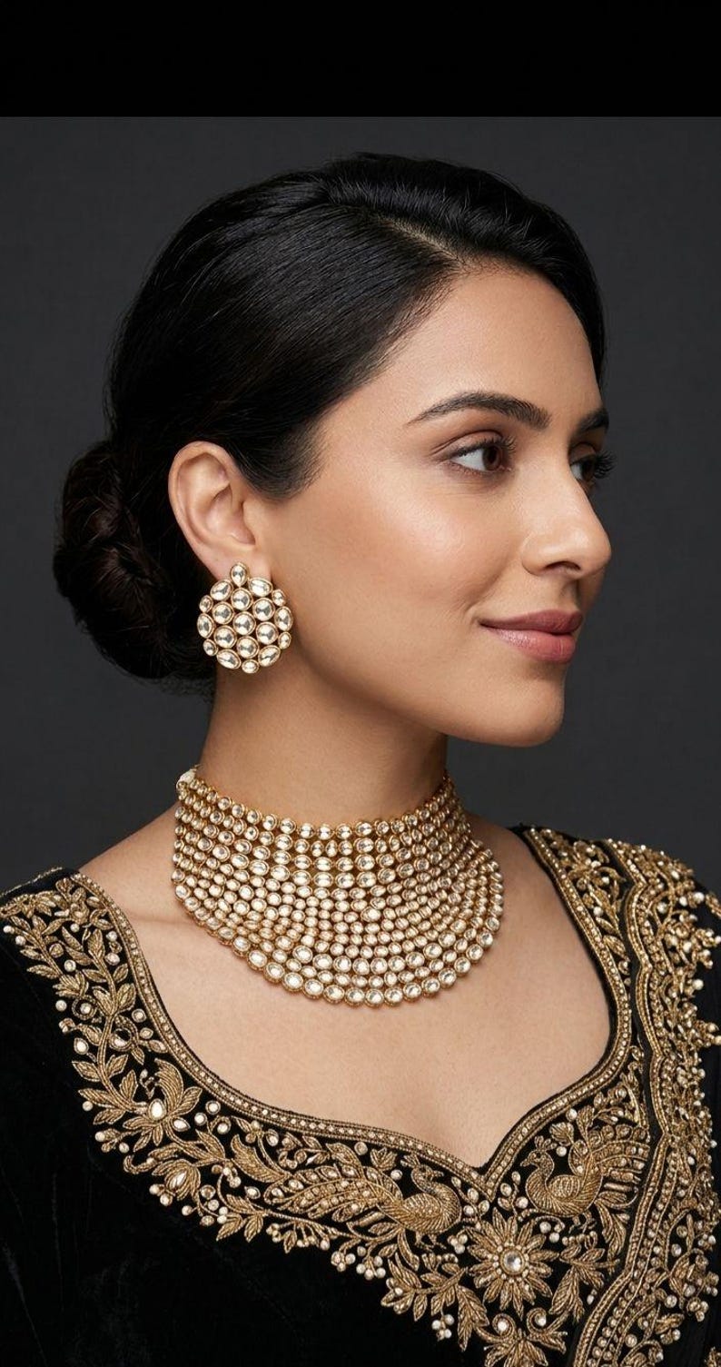 May include: A woman wearing a gold choker necklace and matching earrings. The jewellery is decorated with many small, clear stones. The woman is wearing a black top with gold embroidery.